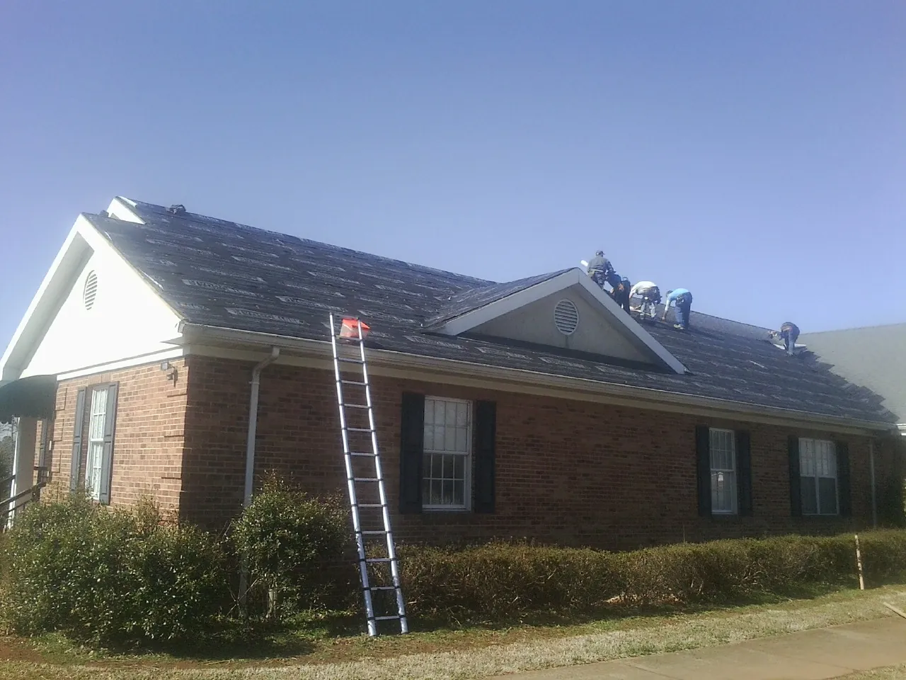 Crew tearing shingles off a brick ranch roof with a ladder set — Metal Roof Repair work by our crew in South Pekin