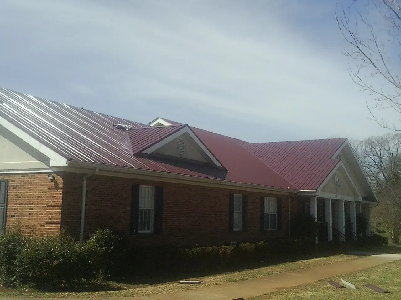 Red metal roof with gabled entries on a long brick building, from a Hail Damage Roof Repair job in South Pekin