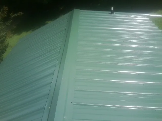 New green metal panels meeting at the ridge of a roof — Flat Roof Repair work by our crew in South Pekin