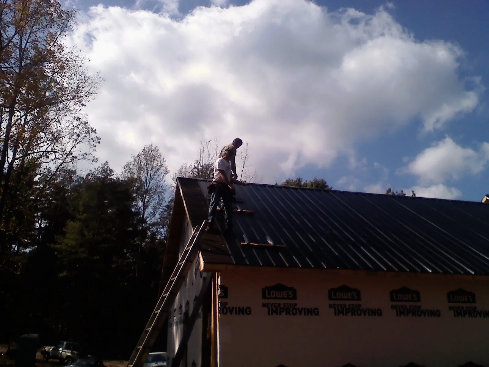 Roofer fastening dark metal panels high against a cloudy sky, from a Roof Inspection job in South Pekin