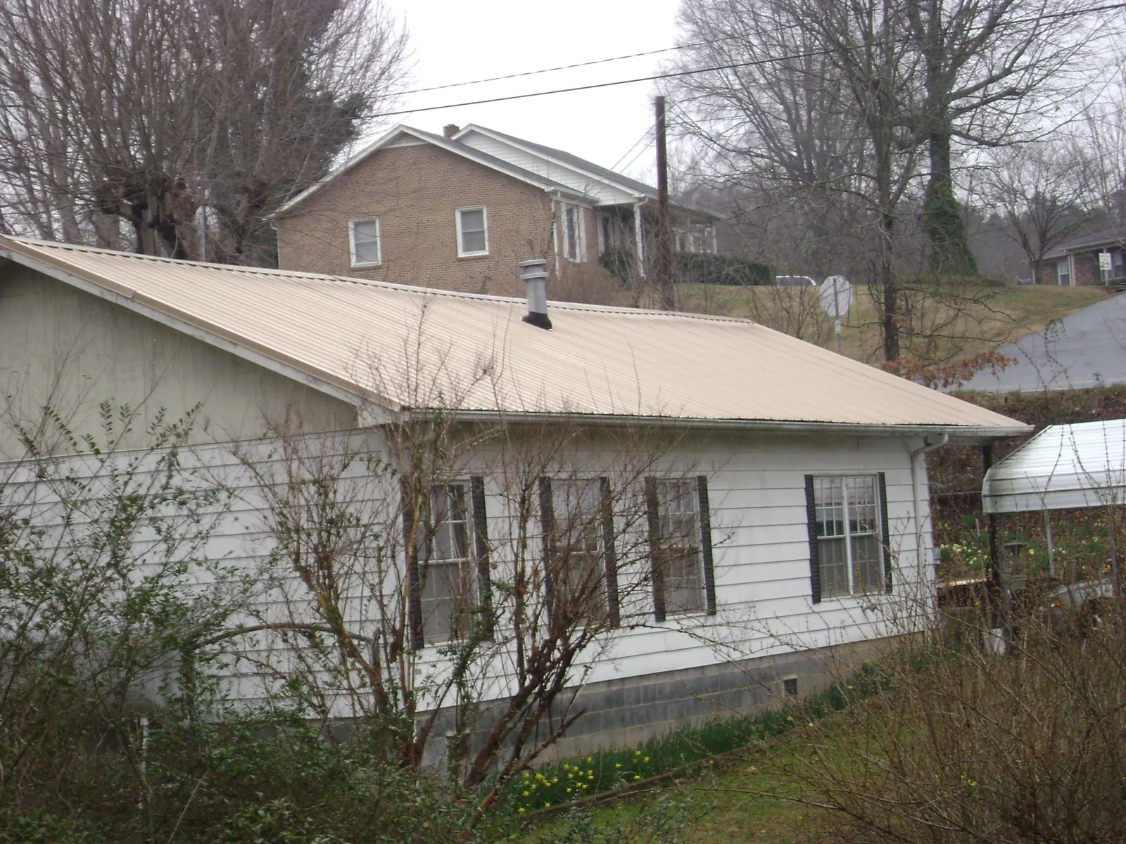 Tan metal roof on a white sided house set into a hillside — Commercial Roofing by Roofing Brothers in South Pekin